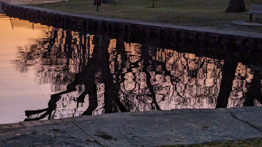 trees and sunset reflected in water between converging banks